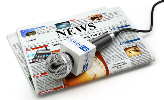 News or journalism concept. Microphone on the newspaper isolated on white.