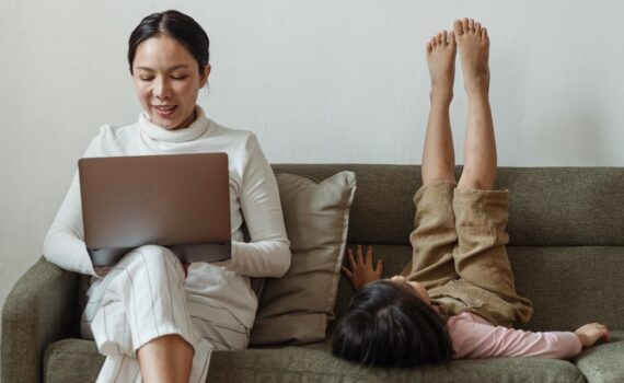 woman using laptop while sitting on couch next to child